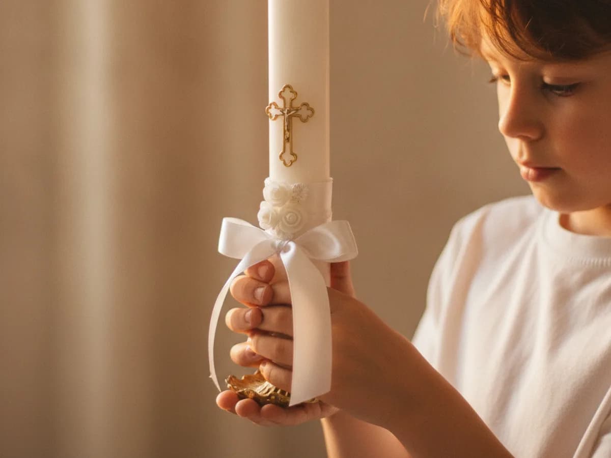 Kommunionkerze in Kinderhänden vor einem Kirchenfenster